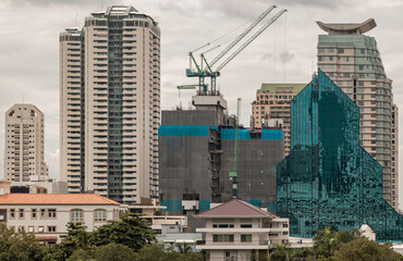 Fototapeta premium Bangkok, Thailand - 10 Sep 2022 : Architectural exterior view of Multiple skyscrapers and Building under construction site with cranes. Conceptual urban building construction, Selective focus.
