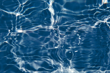 Defocus blurred transparent blue colored clear calm water surface texture with splash, bubble. Shining blue water ripple background. Surface of water in swimming pool. Blue bubble water shining.