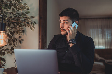 A young guy businessman working at home from his home office and talking on the phone about business