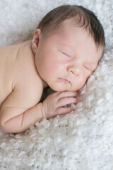 
A cute little baby sleeps on a white bouclé bedspread at home. Health and motherhood