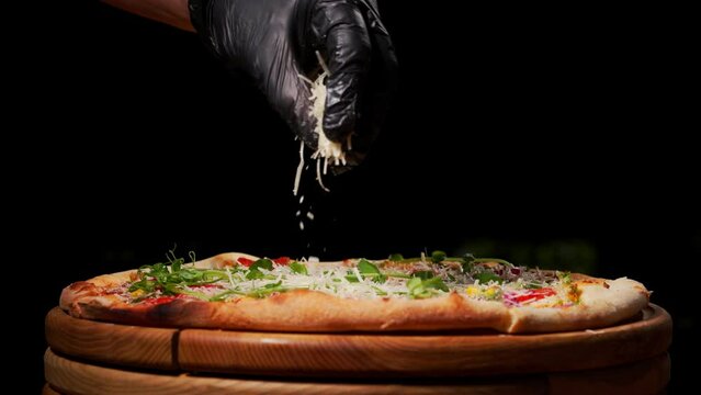 The process of making a large pizza. The hands of the chef in black gloves lay the ham on the grated mozzarella cheese.