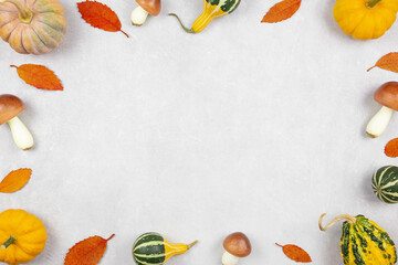 Fall flat lay with colorful pumpkins, mushrooms and fallen leaves on gray concrete background. Autumn mockup border with decoration. Top view. Copy space.