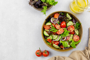 Fresh vegetables salad with cherry tomato, cucumber, lettuce, red onion and olives oil on gray concrete background. Copy space.
