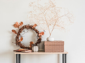 Cozy autumn home interior - a wreath with autumn leaves, dried flowers, craft box, a ceramic pumpkin on a wooden rack in the living room