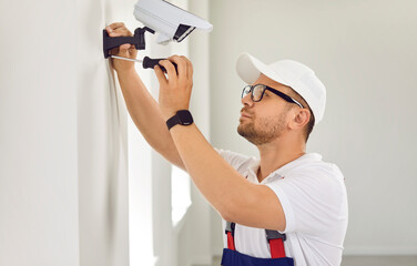 Young man in glasses and white uniform cap uses screwdriver while setting up new security video...