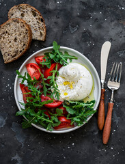 Delicious Italian style salad - fresh burrata, arugula and tomatoes on a dark background, top view