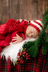 A cute little baby in a red suit and a cap is sleeping in a Christmas decoration. Christmas mood. Happy childhood.