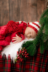 A cute little baby in a red suit and a cap is sleeping in a Christmas decoration. Christmas mood. Happy childhood.