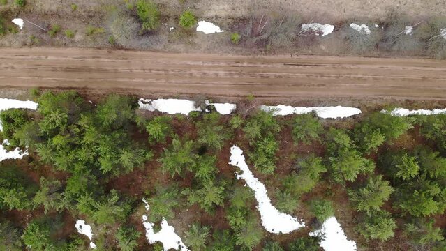 Country gravel road at winter or spring. Snow and green trees. Aerial drone view. Flying over. View from top down. High quality 4k footage