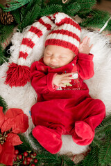A cute little baby in a red suit and a cap is sleeping in a Christmas decoration. Christmas mood. Happy childhood.
