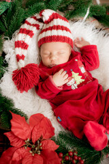 A cute little baby in a red suit and a cap is sleeping in a Christmas decoration. Christmas mood. Happy childhood.