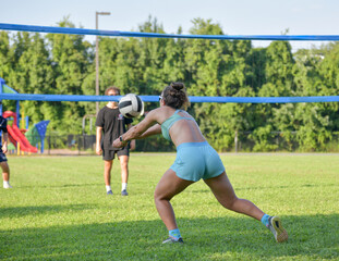 Girl passing the ball during a coed grass doubles game of volleyball on a sunny afternoon
