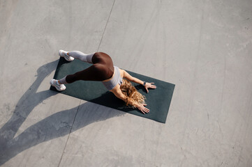 High angle view of the beautiful young woman training outside while standing at the yoga mat