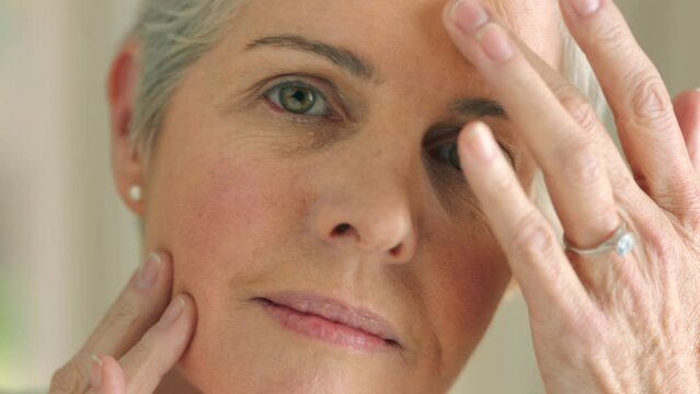 Beauty, face and anti aging with a senior woman touching her face and skin with her hand in a bathroom at home. Skincare, treatment and retirement with an attractive and elderly female pensioner