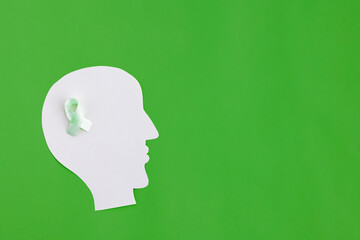 Brain paper cutout with green ribbon on green background with copy space. Mockup for world mental health day