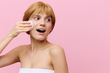 a happy, emotional woman stands on a pink background and wipes her face with a cotton swab, smiling broadly with delight