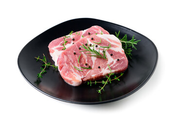 Pieces of pork meat with rosemary and thyme leaves on black dish on white background,