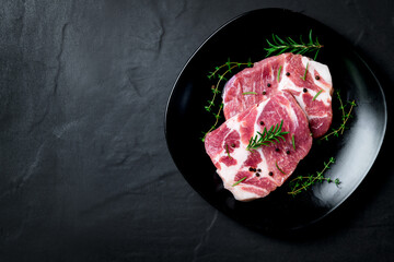 Pieces of pork meat with rosemary and thyme leaves on black dish,