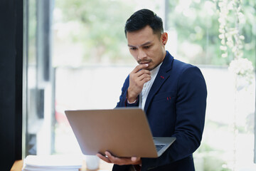 Portrait of an Asian male business owner standing using a computer to analyze work