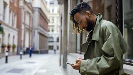 Attractive and stylish young man using his phone as he leans against a wall in the city 