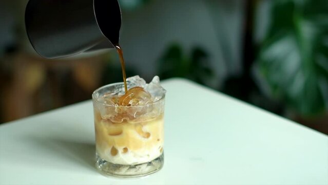 Poured coffee of iced latte coffee into a transparent glass on the white table and monster tree decor backdrop.  shooting photos at home