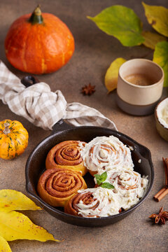 Pumpkin cinnamon rolls. Yeast dough buns in a shape of spiral with sugar and cinnamon filling and cream cheese frosting. Delicious autumn homemade dessert.