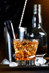 Godfather alcoholic cocktail with scotch whiskey, amaretto liqueur and ice. Black bar counter background, steel bar tools, copy space