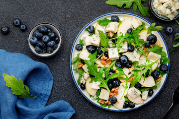 Delicious arugula salad with pears, blueberries, roquefort cheese and walnuts. Black kitchen table background, top view