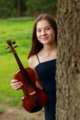 beautiful girl with violin peeking out from behind a tree