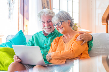 Cute couple of seniors watching movies having fun using laptop at home sitting on the sofa...