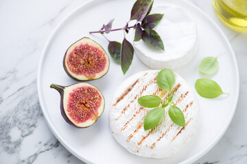 White plate with grilled camembert cheese, fig fruits and fresh basil, middle close-up, elevated view