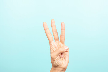 Hand gesture. Female hand shows number three. Woman hand pointing up with three fingers on light blue background