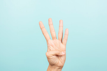 Hand gesture. Female hand shows number four. Woman hand pointing up with three fingers on light blue background