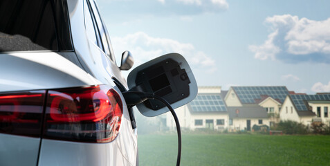 Close up of electric car inlet with a connected charging cable on a background of green city using renewable solar energy