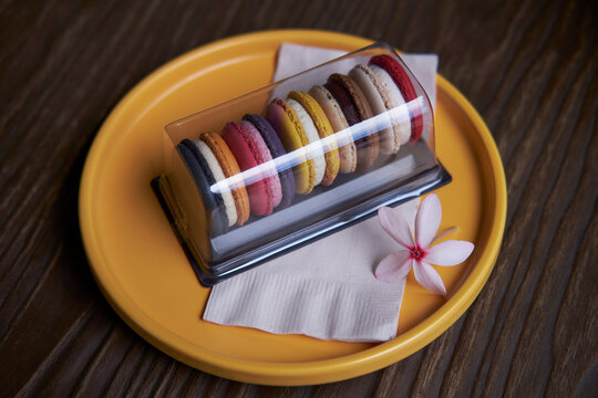 Variety of colorful french sweet dessert macaron in packaging in the orange seramic plate on the table