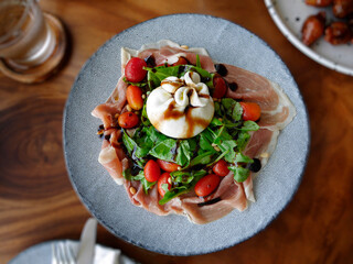 Directly above, Close up of Fresh Salad, Burrata Cheese topping on Prosciutto, Arugula and tomato,...