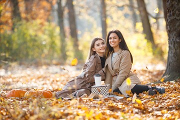 Two girls making picnic on a blanket in autumn park