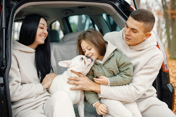 Young family sitting at open trunk of hatchback car in autumn forest