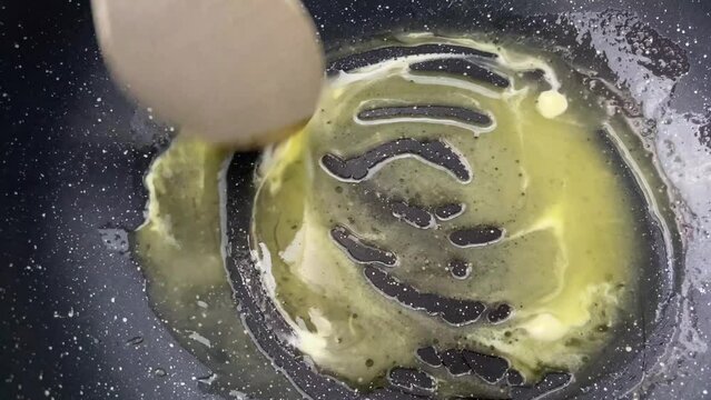 Preparing farofa (Brazilian toasted cassava flour) toasting in a pan on the electric stove. Butter piece is melted in a frying pan, while stirred by a wooden spoon.