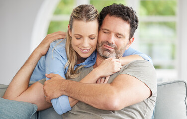 Couple, love and hug with a man and woman hugging in the living room of their home. Relax, together and happy with a female and male embracing for affection, romance and bonding on the house sofa