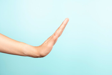 Woman hand gesture. Female hand show stop sign gesture on light blue background. Front view, copy space.