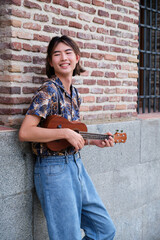 Young Taiwanese man smiling and playing acoustic Ukulele guitar at street.