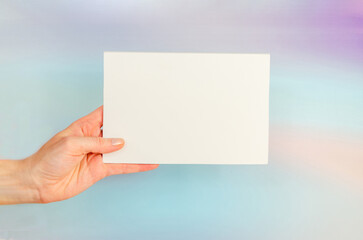 Fototapeta premium woman's hand holds white blank sheet on blue background. Copy space, text space. Layout template