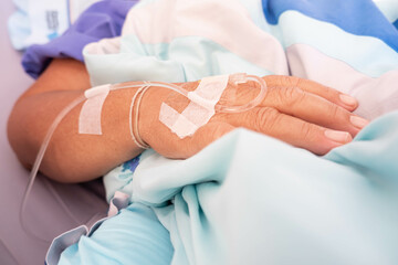 Close up on hand with saline solution of elderly woman patient sleeping on the bed In the hospital.