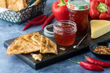 Jars of fresh hot pepper jelly on a board with cheese and crisp cracker bread.