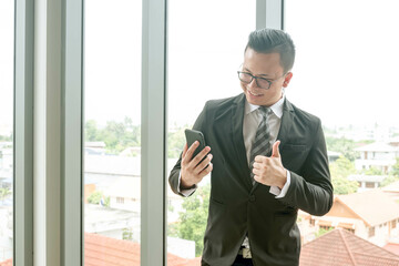 Happy asian businessman watching smartphone show thumbs up sight in office