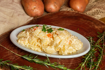 A delicious homemade creamy potato salad served on a white plate in a rustic setting with fresh ingredients in the background.