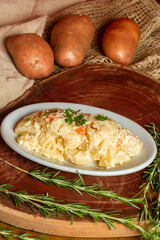 A delicious homemade creamy potato salad served on a white plate in a rustic setting with fresh ingredients in the background.
