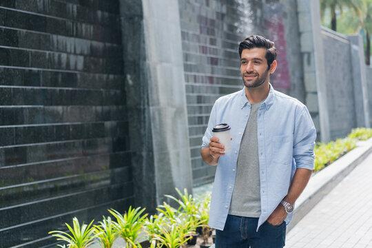 portrait of stylish handsome young man standing outdoor , Smiling man with glasses holding cup of coffee and using mobile phone