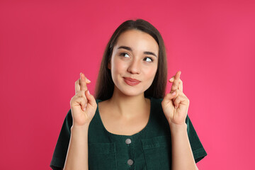 Woman with crossed fingers on pink background. Superstition concept